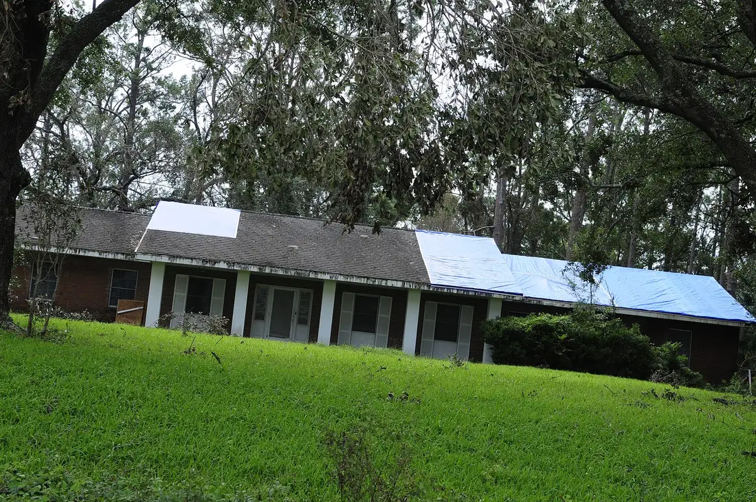 Blue tarps covering part of the storm-damaged shingle roof of a single-story brick house