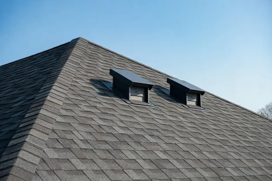 Two black box vents near the ridge of a gray asphalt shingle roof