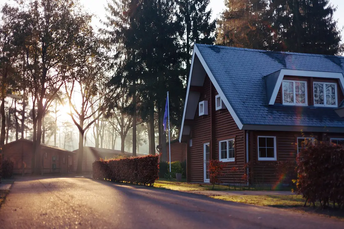 Brown wood-sided house with a gray shingle roof and white-trimmed dormers in early morning sunlight