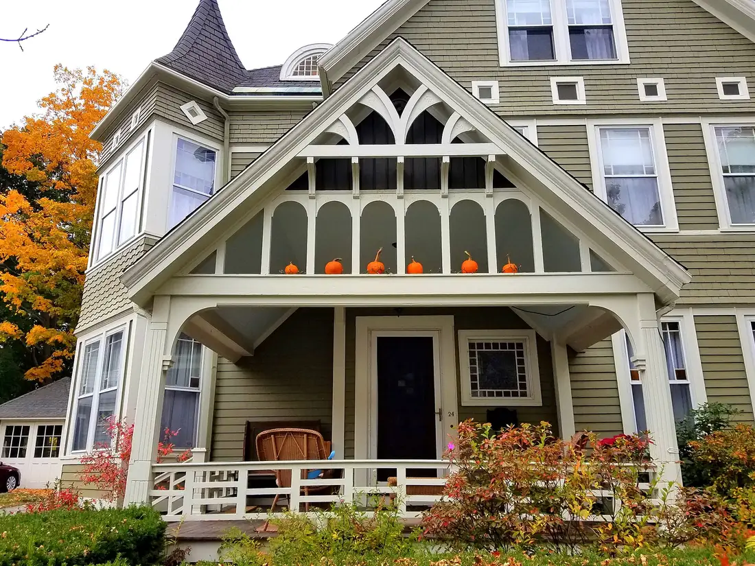 Covered front porch with a decorative gable roof on a green Victorian house in autumn