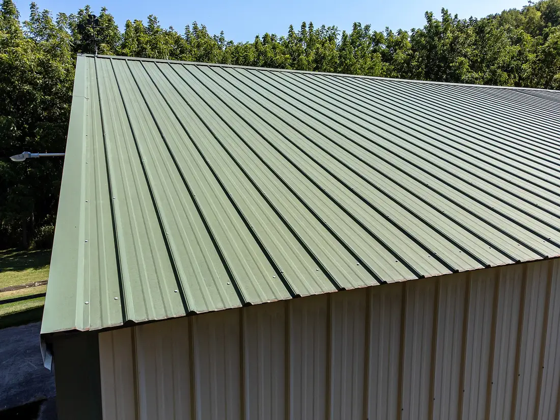 Green corrugated metal roof on a pole building with light-colored metal siding