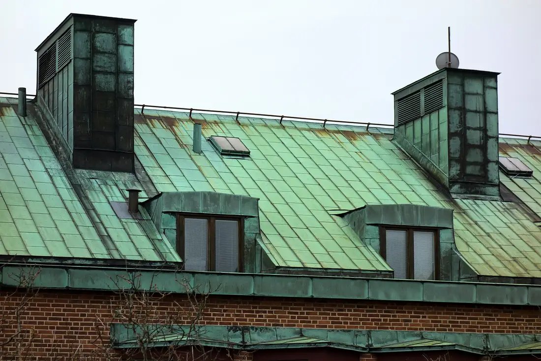 Green patinated copper roof with dormer windows and copper-clad chimneys above a brick wall